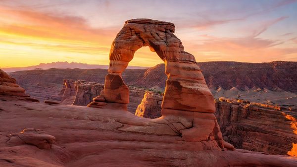 Delicate Arch at sunrise, orange sandstone against blue Utah sky
