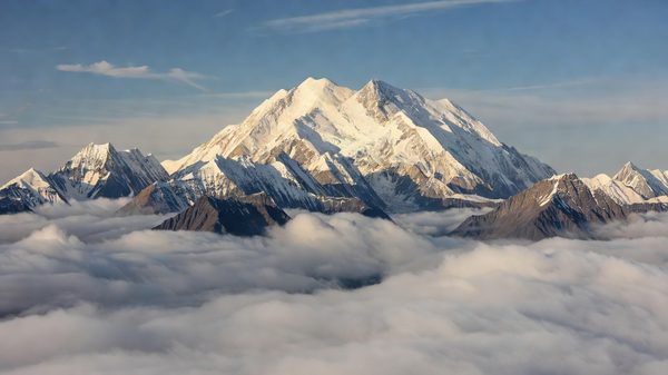 Snow-capped Denali summit above clouds with Alaska tundra below
