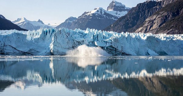 Tidewater glacier calving into Glacier Bay, Alaska, with mountain reflections in calm fjord water