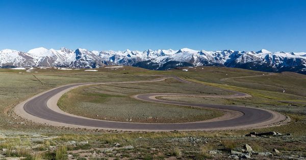 Trail Ridge Road winding through alpine tundra above treeline at Rocky Mountain National Park, Colorado, with a panorama of snow-capped peaks under a deep blue sky