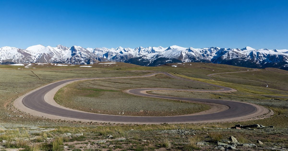 Trail Ridge Road winding through alpine tundra above treeline at Rocky Mountain National Park, Colorado, with a panorama of snow-capped peaks under a deep blue sky